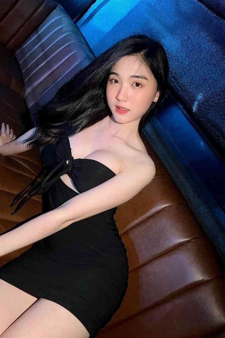 Beautiful Asian woman in black dress reclining on a brown leather couch, looking at the camera.