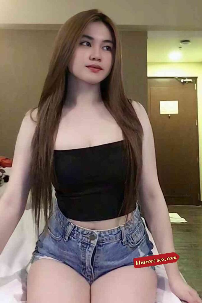 Attractive Asian woman in black top and denim shorts, posing indoors with long brown hair.