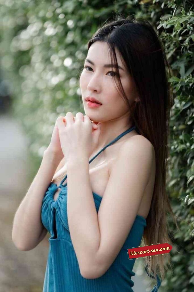 Beautiful Asian woman in blue halter top posing outdoors with hands clasped. Natural light, soft focus.