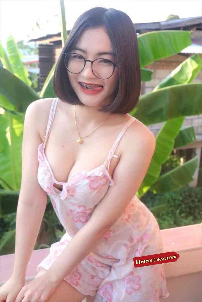 Smiling Asian woman with braces, wearing glasses and floral pajamas. Banana leaves in background.