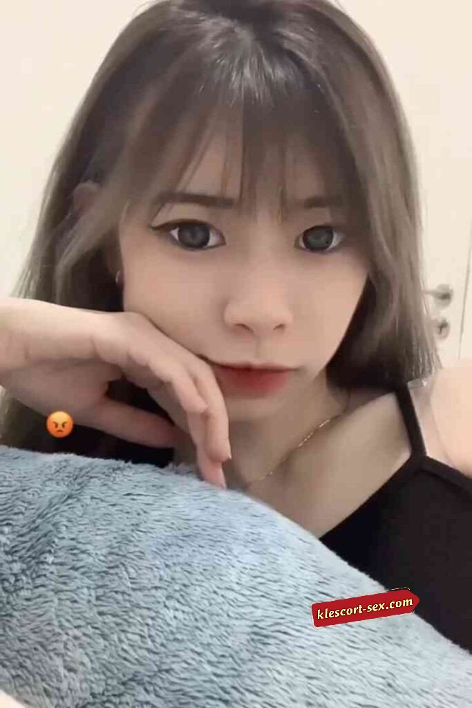 Asian woman with grey-brown hair, black top, resting chin on hand.