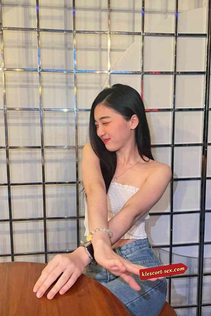 Smiling Asian woman in tube top and jeans sitting at table.