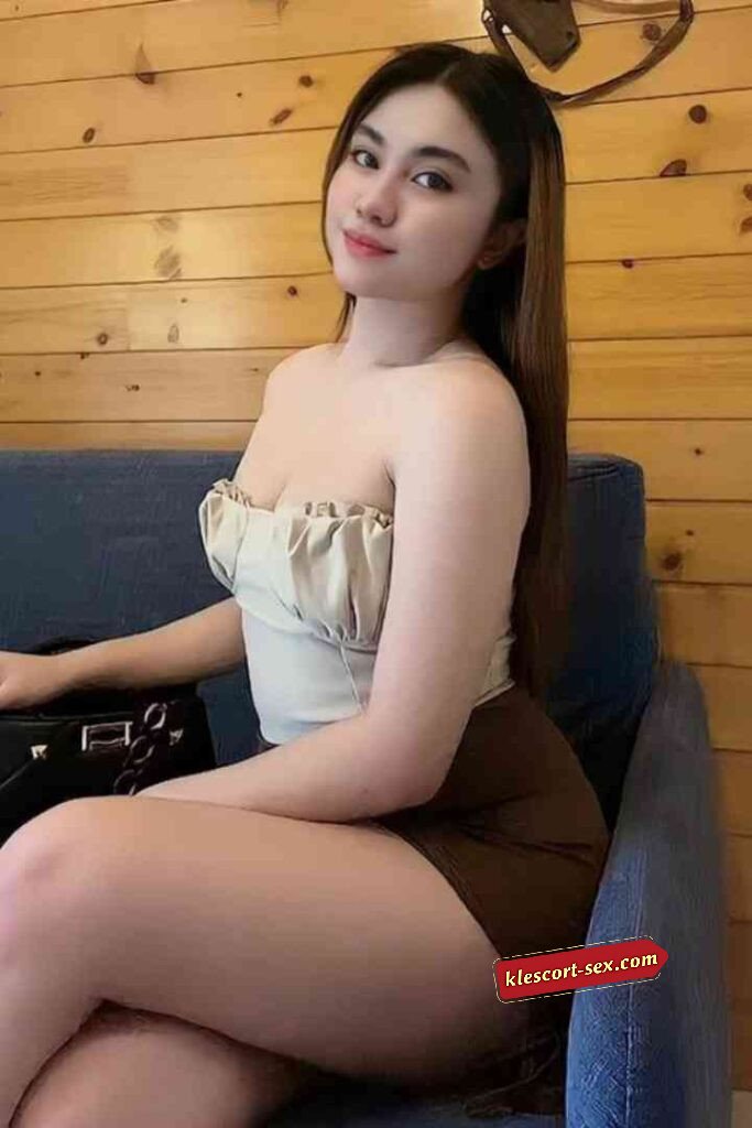 Attractive Asian woman in tube top and skirt sitting on blue couch against wood paneling.