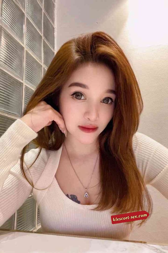 Portrait of a beautiful woman with auburn hair and a white top, wearing a delicate necklace.