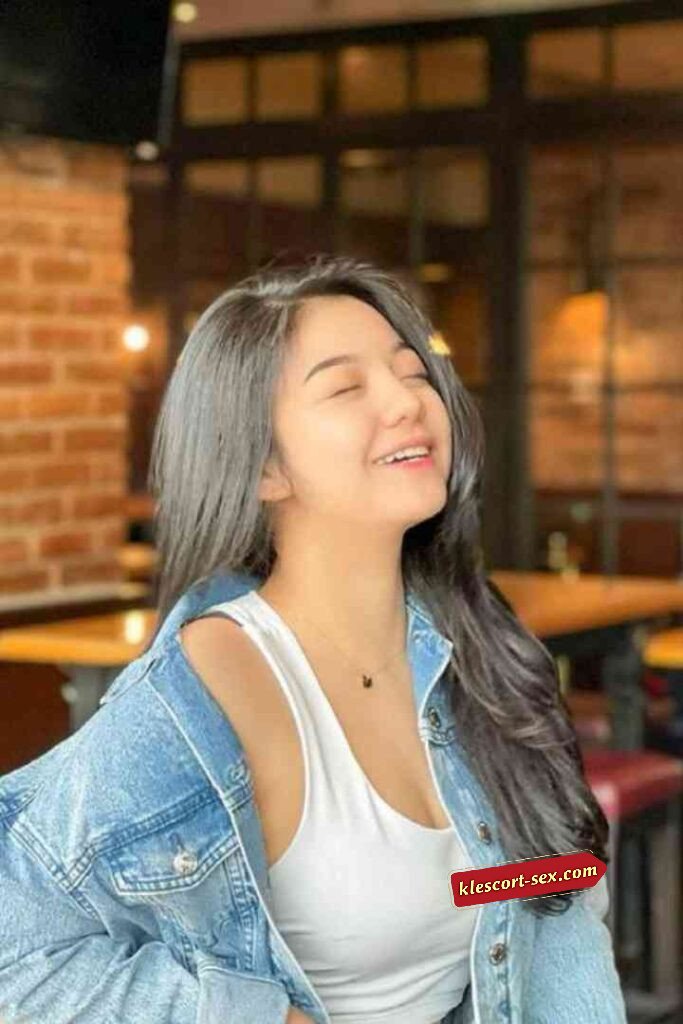 Smiling Asian woman in denim jacket and white top. Indoor cafe setting, warm lighting.