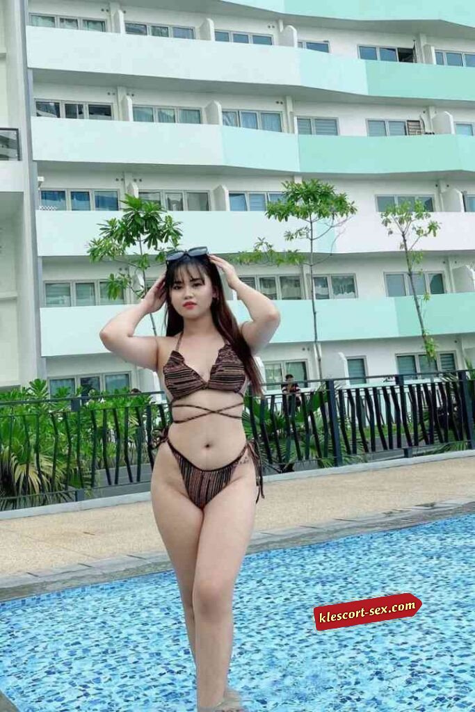 Woman in bikini by pool with sunglasses on head smiling.