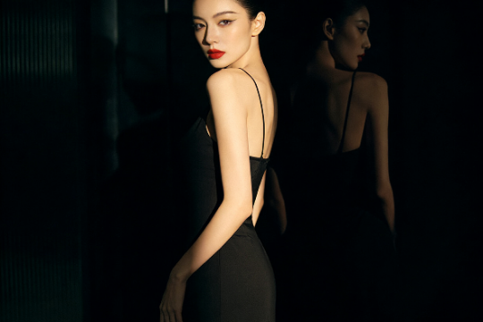 Elegant woman in black dress, red lipstick, glancing over shoulder.