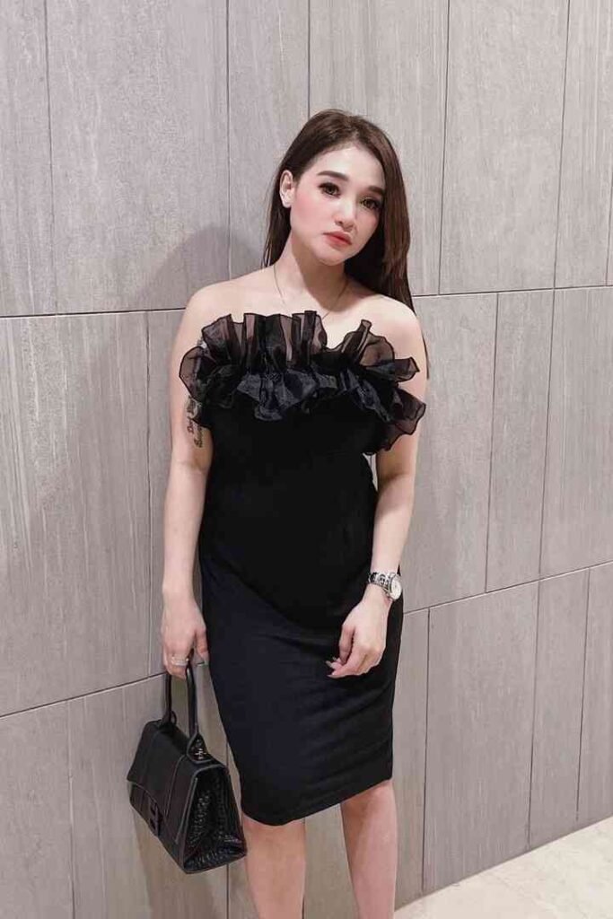 Woman in elegant black dress with ruffle detail poses indoors.
