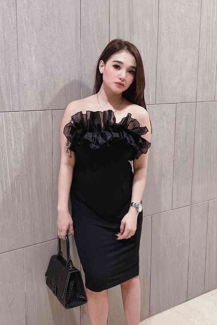 Woman in elegant black dress with ruffle detail poses indoors.