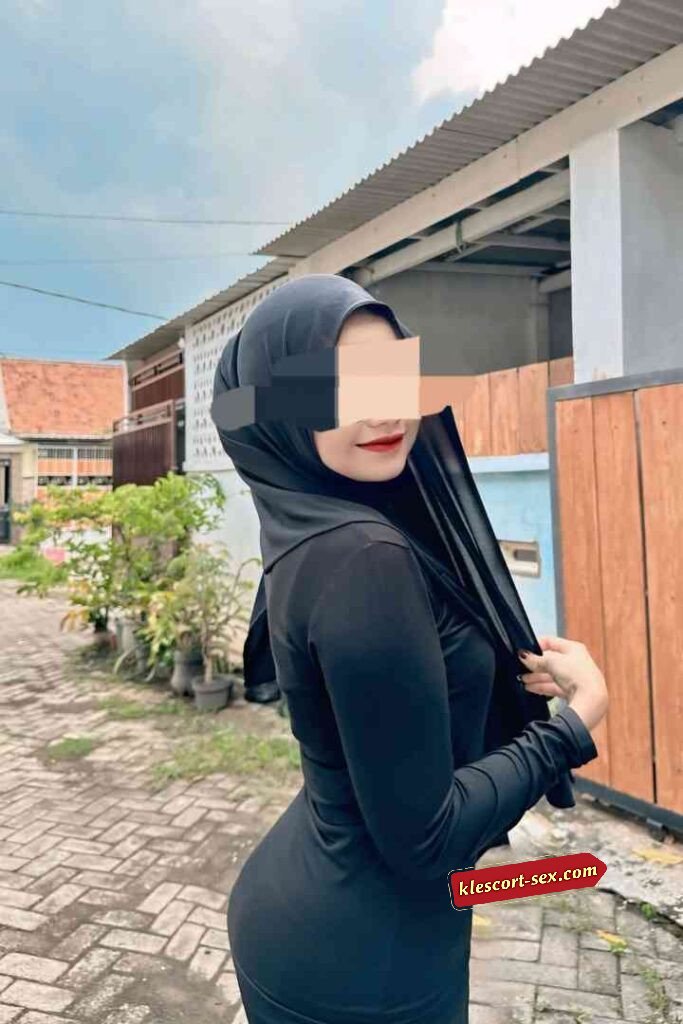 Woman in black hijab and dress poses outside.