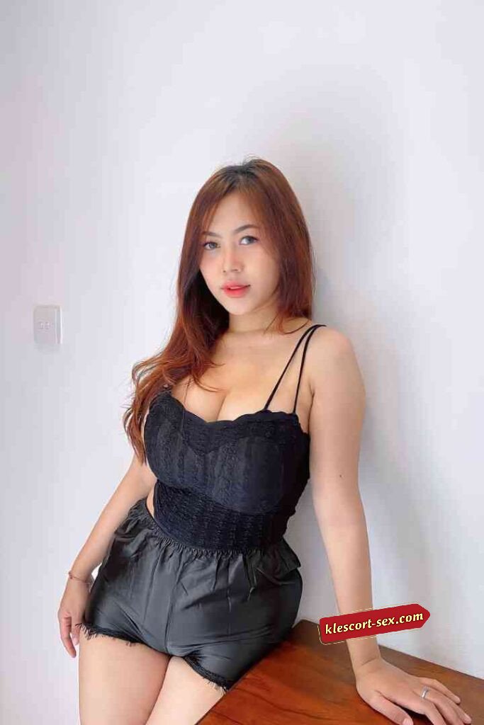 Woman in black lace top and shorts leaning against wall.