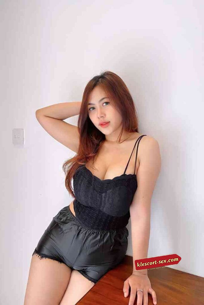 Beautiful woman in black lace top and shorts posing against a white wall.