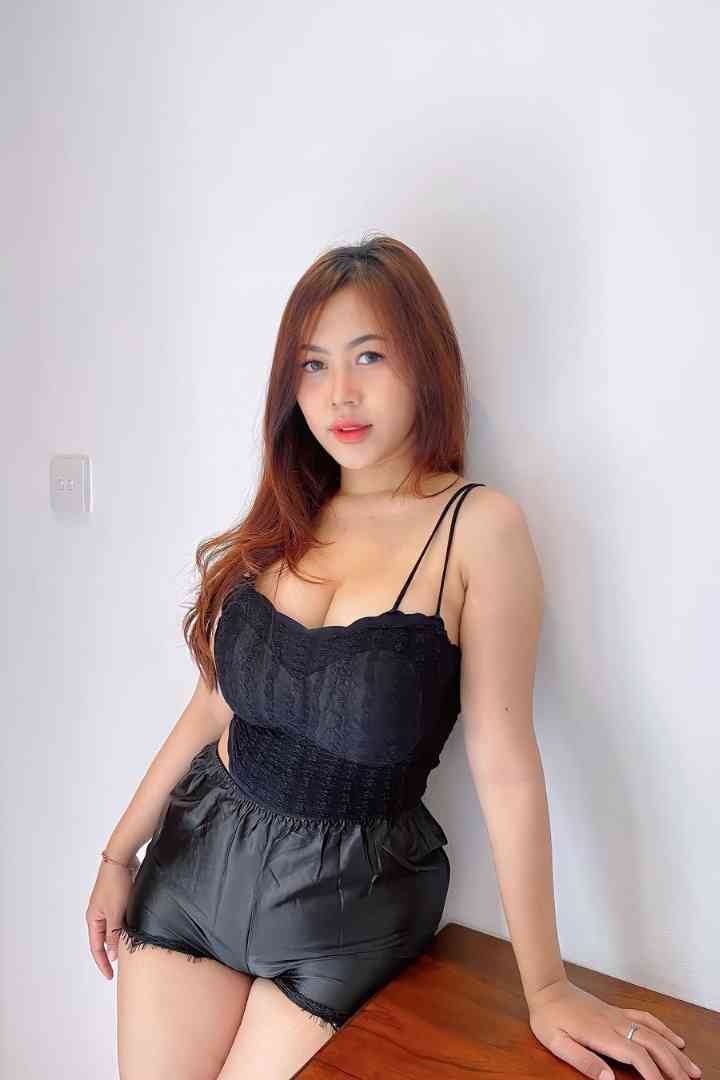 Woman in black lace top and shorts leaning against wall.