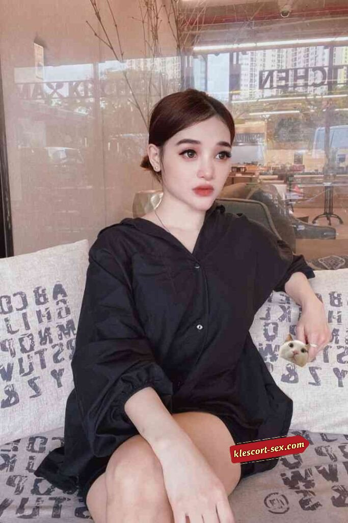 Woman in black shirt sitting on couch, looking away, soft lighting.