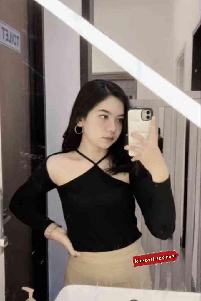 Young woman in black top takes selfie in mirror.