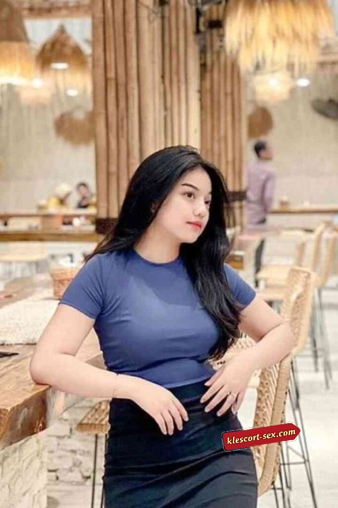 Young woman in blue top and black skirt leaning on counter.
