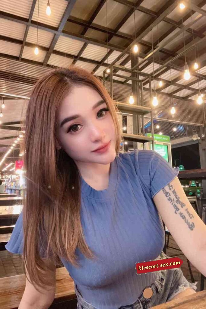 Attractive woman with brown hair in blue top and denim shorts smiling.