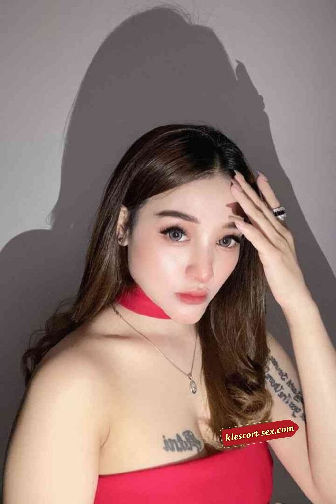 Attractive woman with brown hair and shoulder tattoo posing with hand near face.