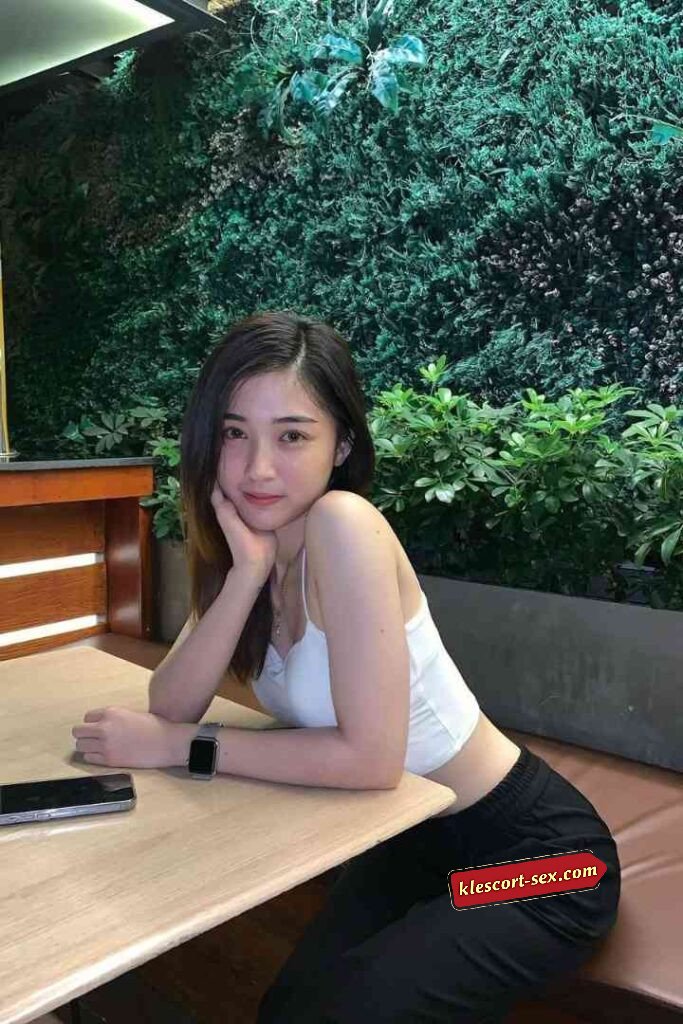 Woman in white top and black pants at cafe table with phone and watch.
