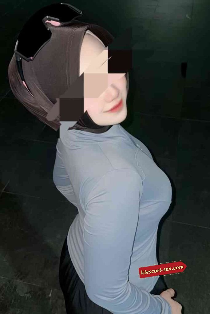 Woman in hijab and athletic wear, posing in dimly lit area. Modest fashion and fitness concept.