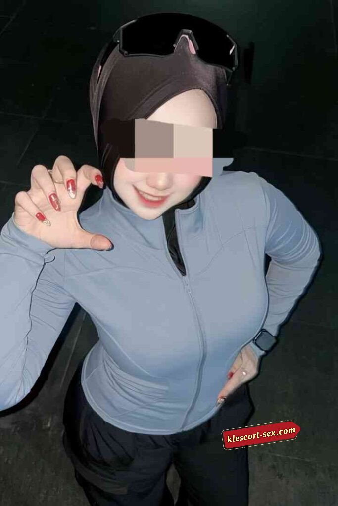 Woman in hijab and athletic wear making a small gesture with her fingers.