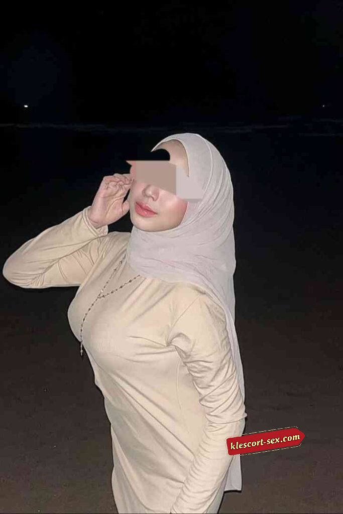 Woman in hijab at night on beach, wearing a long-sleeved dress.