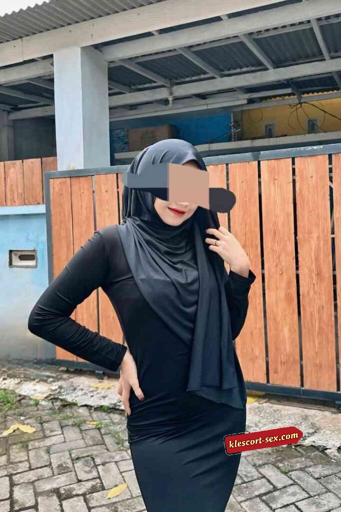 Woman in hijab and black dress posing outdoors.