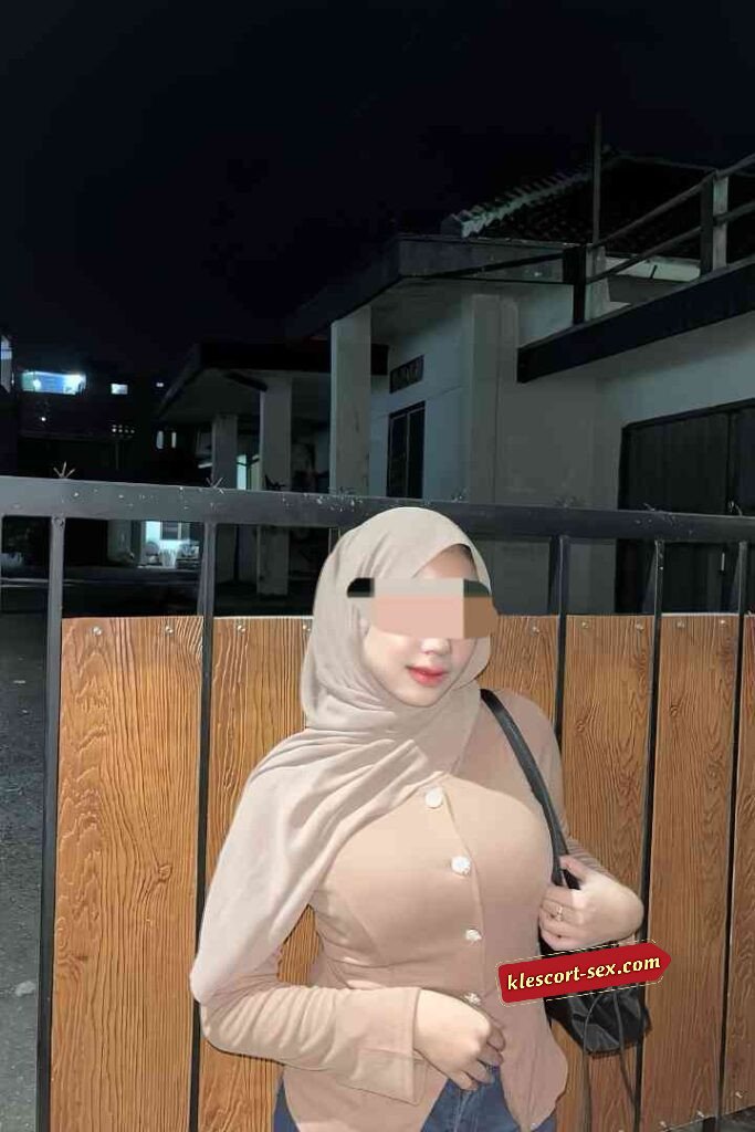 Woman in hijab and blouse poses outdoors at night.