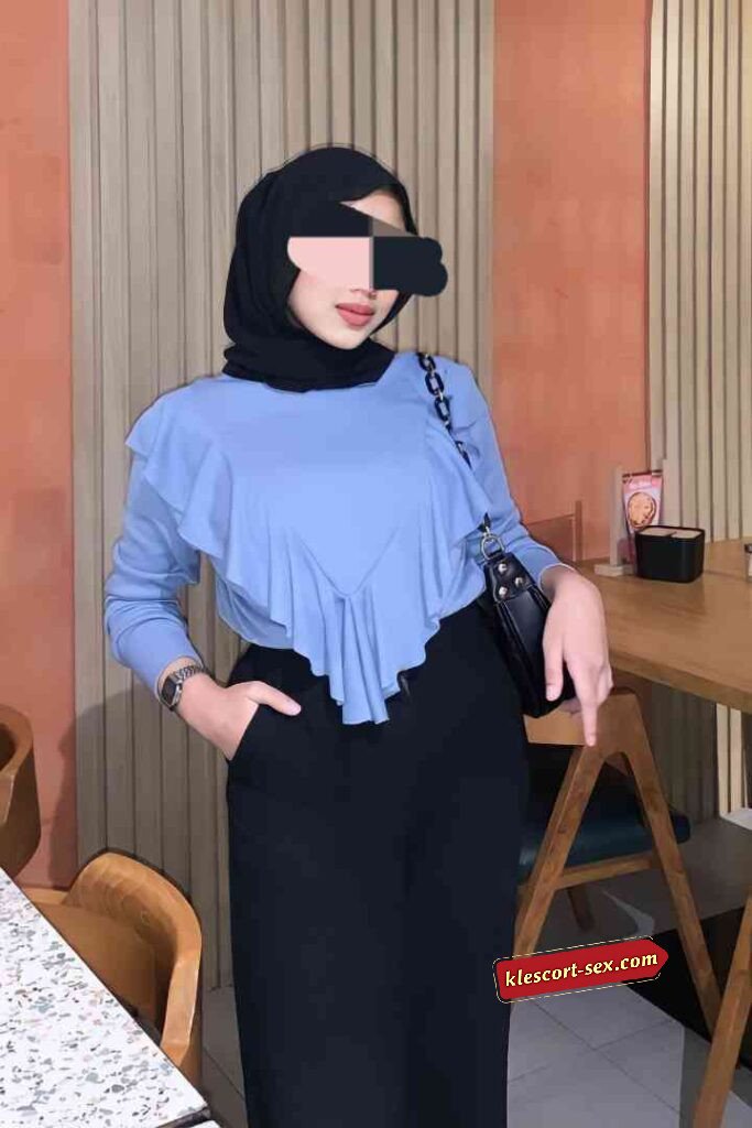 Woman in hijab wearing blue ruffle top and black pants.