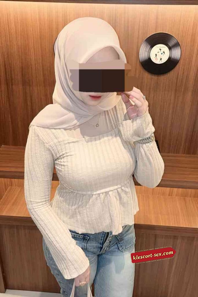 Woman in hijab, cream top, and jeans posing indoors.