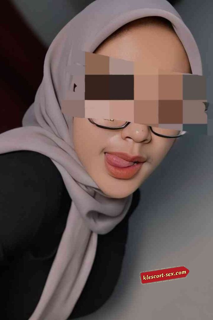 Woman in hijab with glasses sticking tongue out.