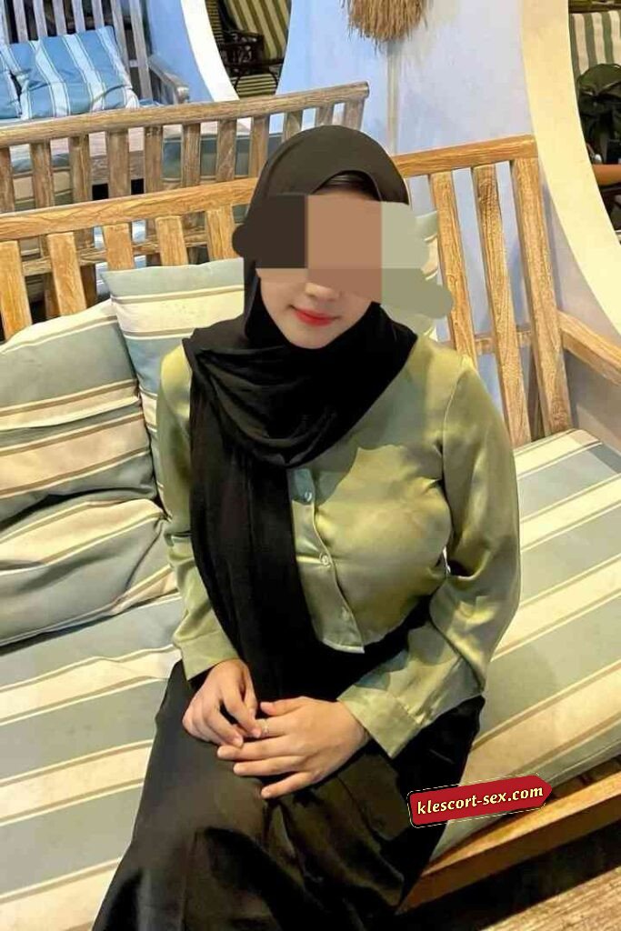 Woman in hijab sitting on striped cushion bench.