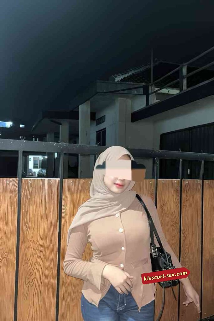 Woman in hijab and jacket posing outdoors at night.