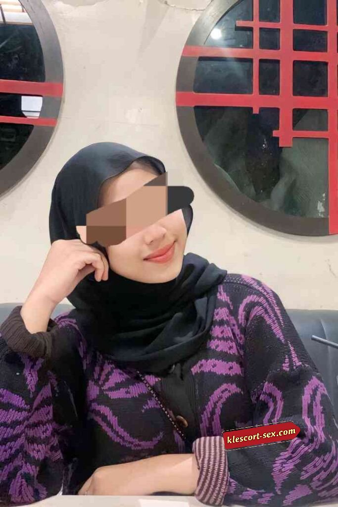 Woman in hijab and patterned sweater smiling indoors.