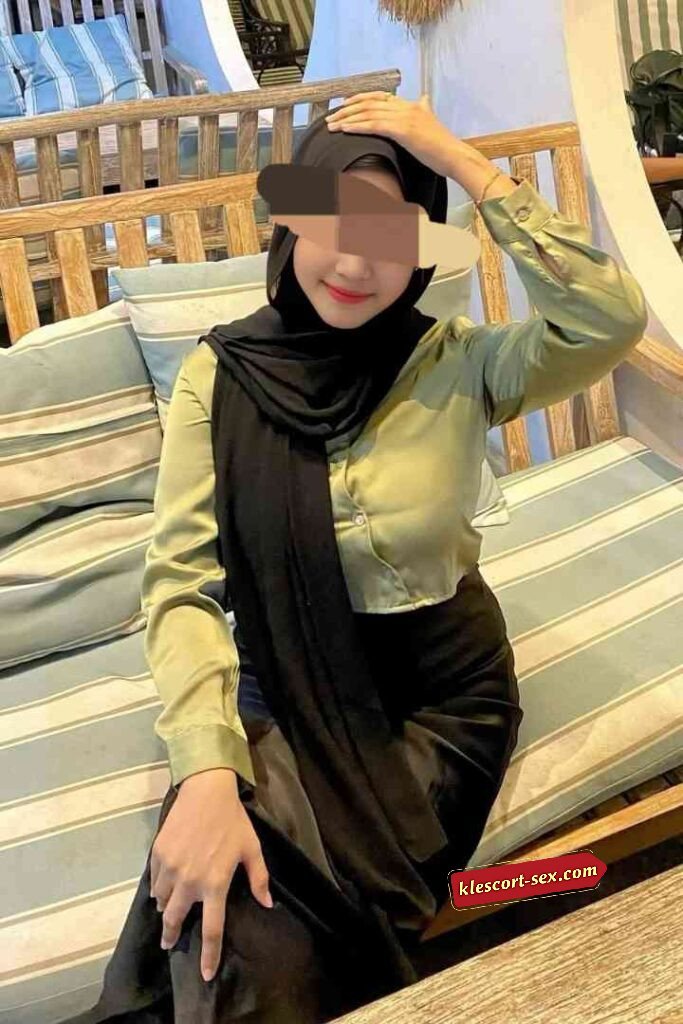 Woman in hijab and satin outfit poses on a bench.