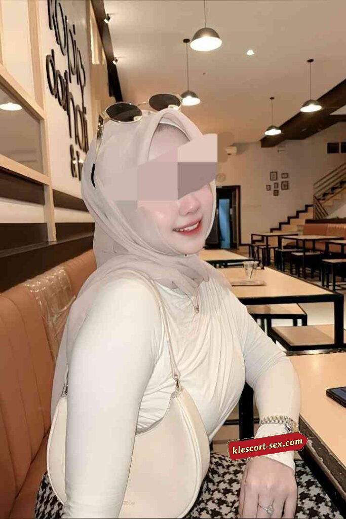 Woman in hijab with sunglasses, cream top, and handbag in restaurant setting.