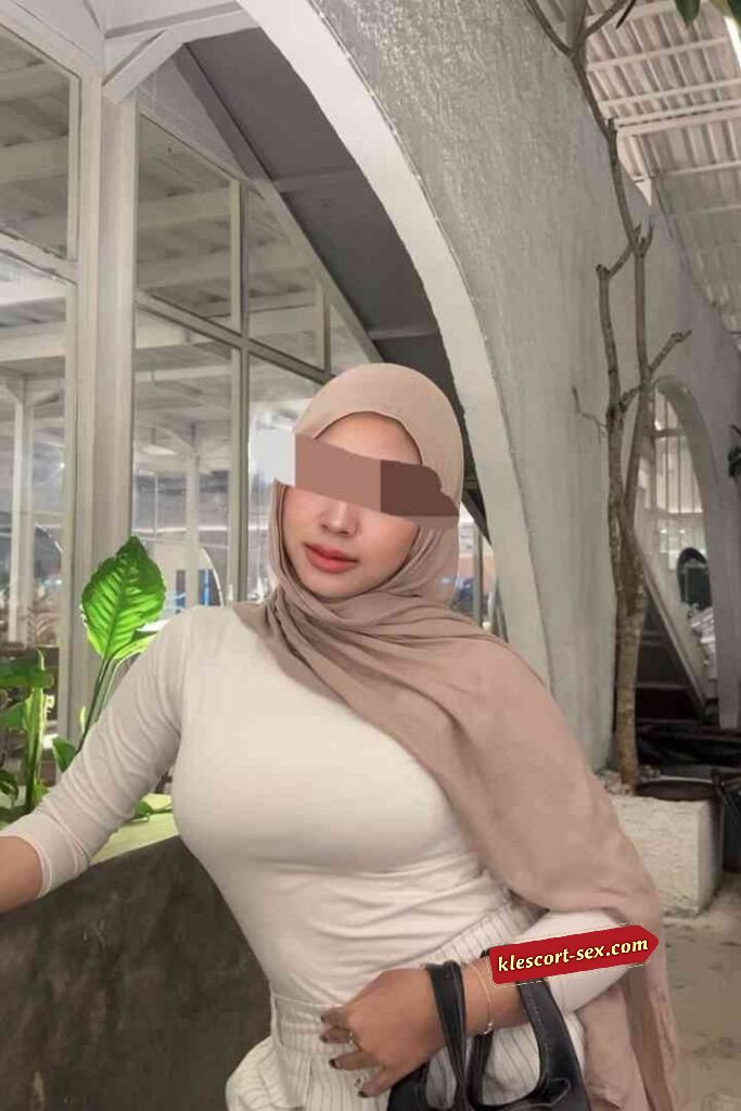 Woman in hijab with white top and skirt, posing indoors.