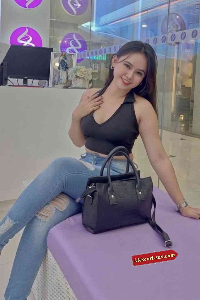 Smiling woman in jeans and black top with handbag sitting indoors.