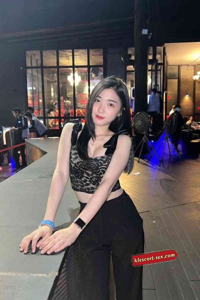 Woman in lace top and black pants posing outdoors at night.