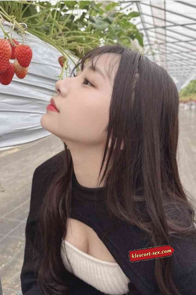 Woman looking at strawberries in greenhouse, wearing black top.