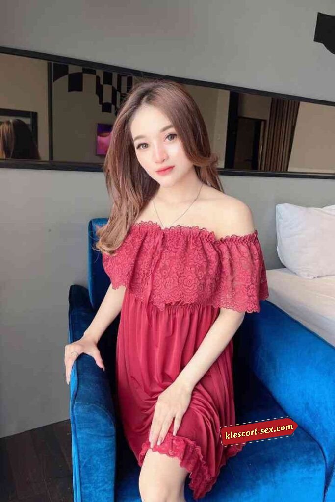 Attractive woman in red off-shoulder dress sitting on blue chair.