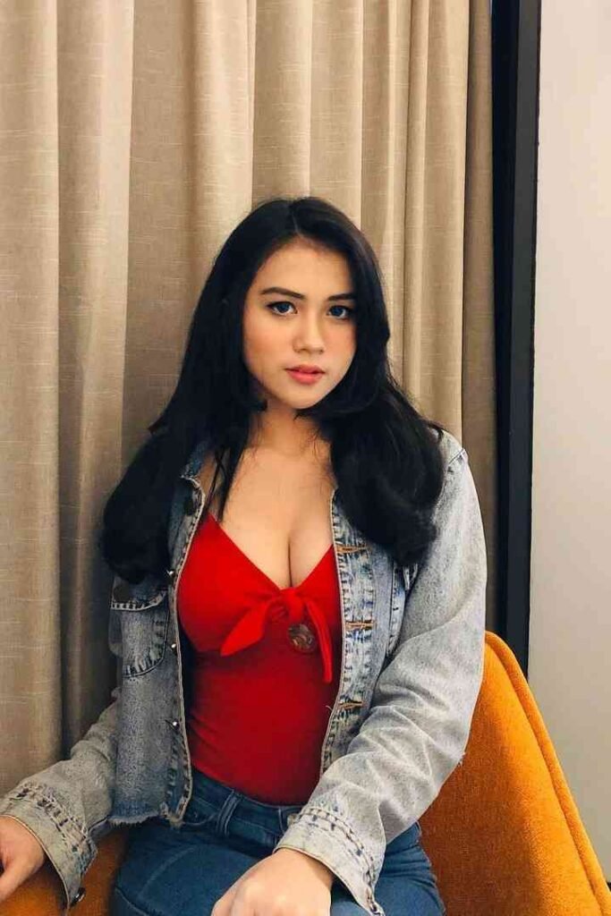 Attractive woman in red top and denim jacket sitting indoors.