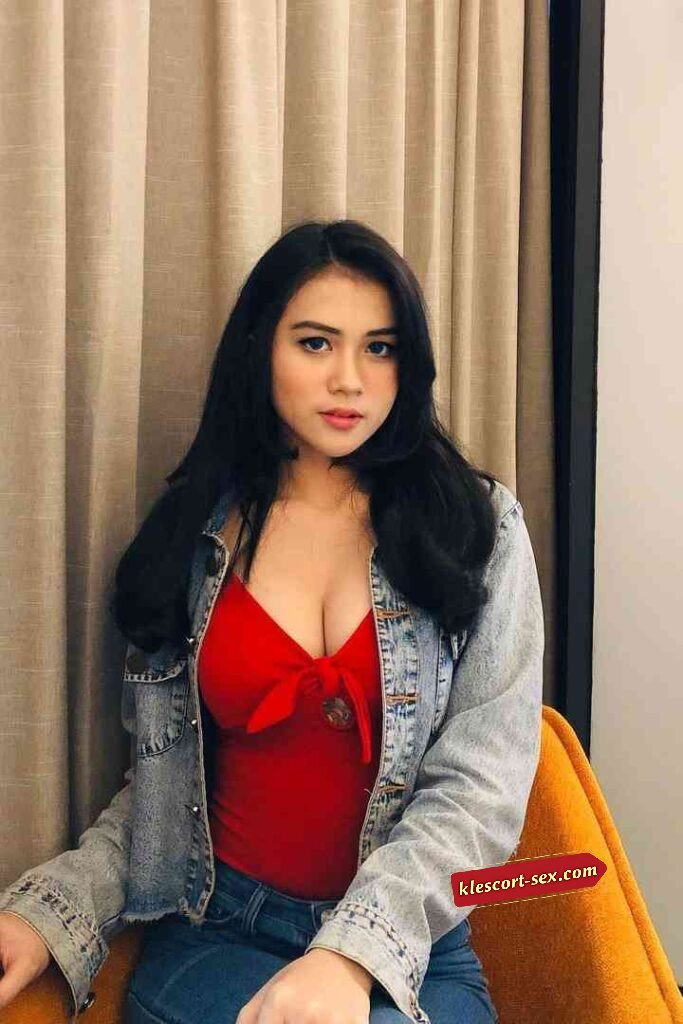 Attractive woman in red top and denim jacket posing indoors.