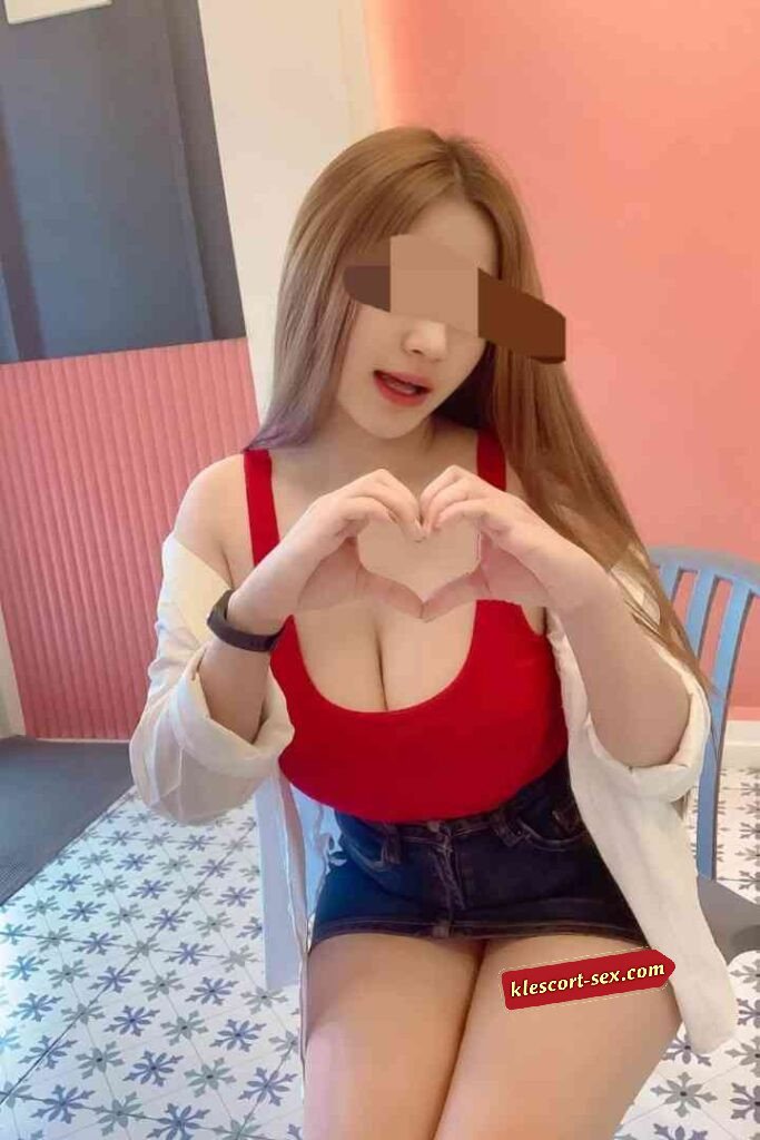 Woman in red top makes heart shape with hands. Casual pose, smiling.