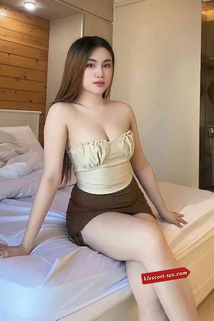 Attractive woman in tube top and skirt sitting on bed. Brunette woman with fair skin posing indoors.