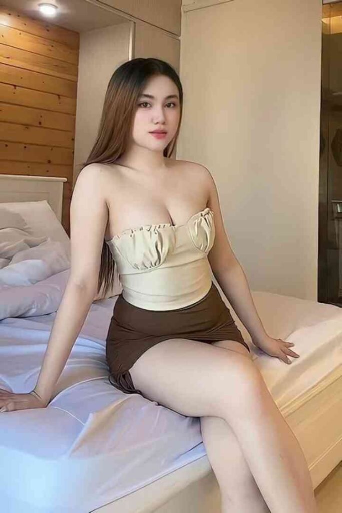 Woman in tube top and skirt sitting on bed. Brunette with fair skin posing indoors.