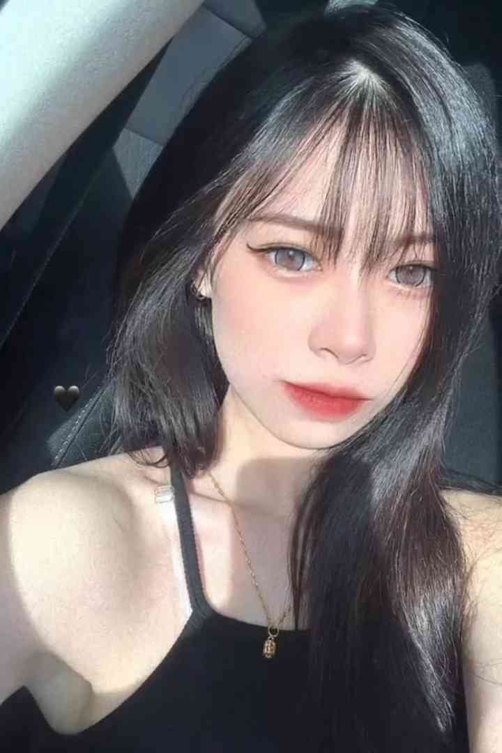 Young woman with black hair and bangs wearing a black top and necklace, looking at the camera.