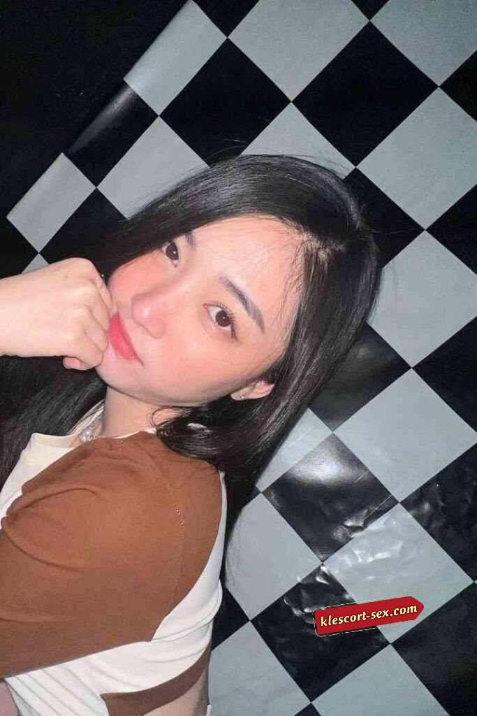 Portrait of a young woman with long black hair posing against a black and white checkered background.