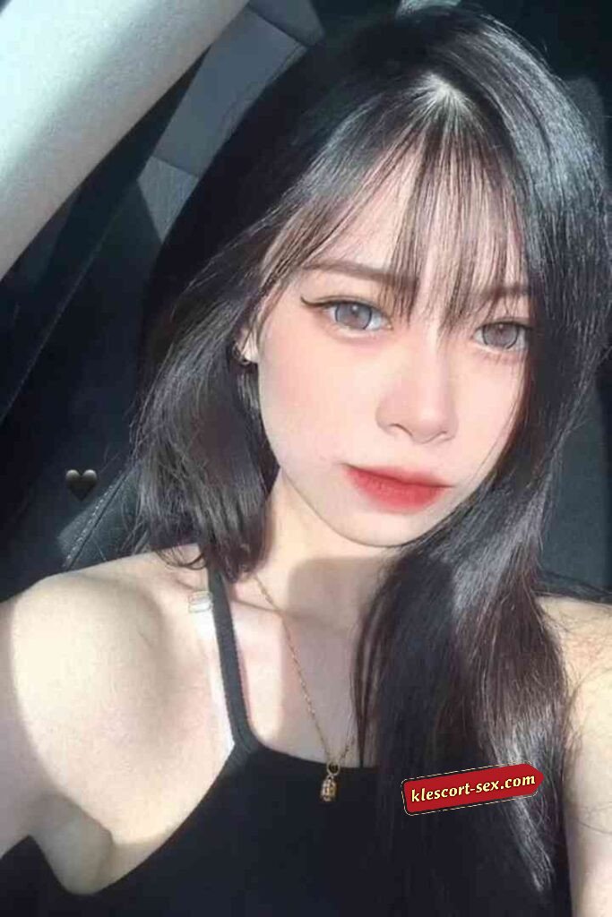 Young woman with black hair, bangs, gray eyes, and red lipstick wearing a black top.