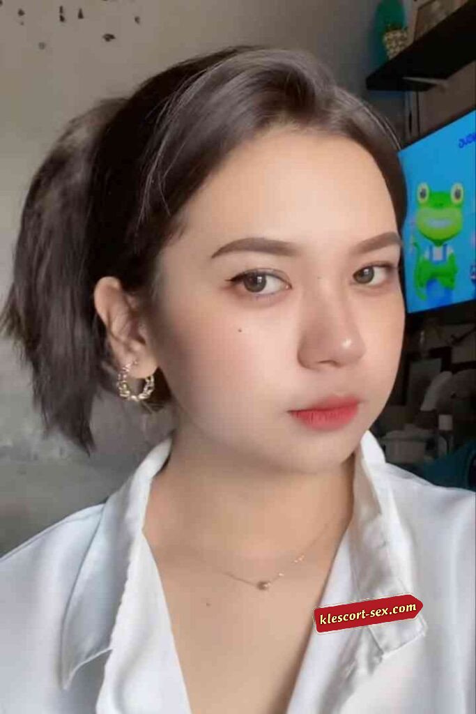 Portrait of a young woman with short brown hair, gold earrings, and a simple gold necklace. Red lipstick.